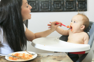 Mother feeding hungry six month old baby solid food